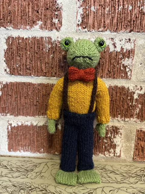 Hand-knitted green frog wearing a mustard cardigan and red bow tie