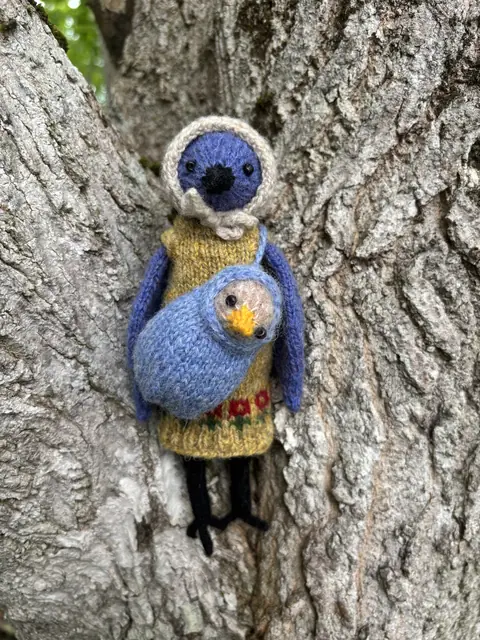 Hand-knitted blue and white bird carrying a small yellow chick