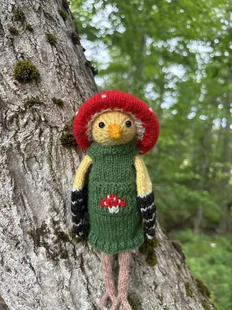 Hand-knitted bird with red hair wearing a green dress with a mushroom pocket