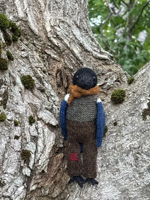 Hand-knitted bird with blue wings wearing brown overalls