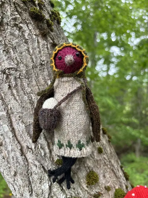 Hand-knitted bird wearing a cream dress with green embroidery