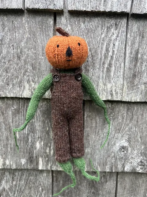 Hand-knitted creature with a pumpkin head and long green arms